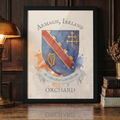 A framed art print featuring the Armagh, Ireland coat of arms with the name 'ORCHARD' below, styled on a wooden table next to a lit brass lamp and books.
