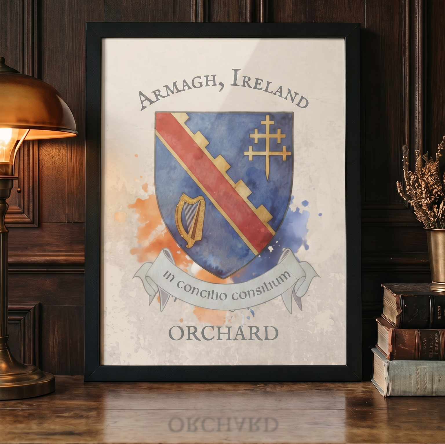 A framed art print featuring the Armagh, Ireland coat of arms with the name 'ORCHARD' below, styled on a wooden table next to a lit brass lamp and books.