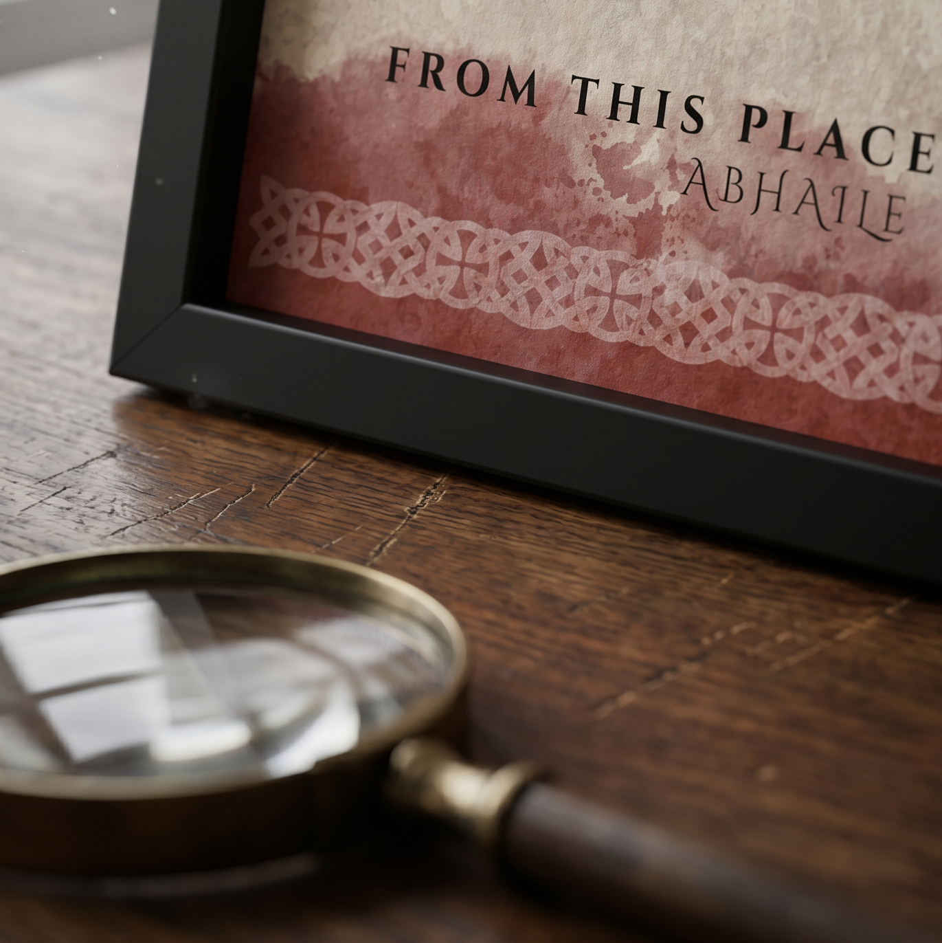 Framed text 'FROM THIS PLACE ABHAILLE' with a magnifying glass on a wooden surface